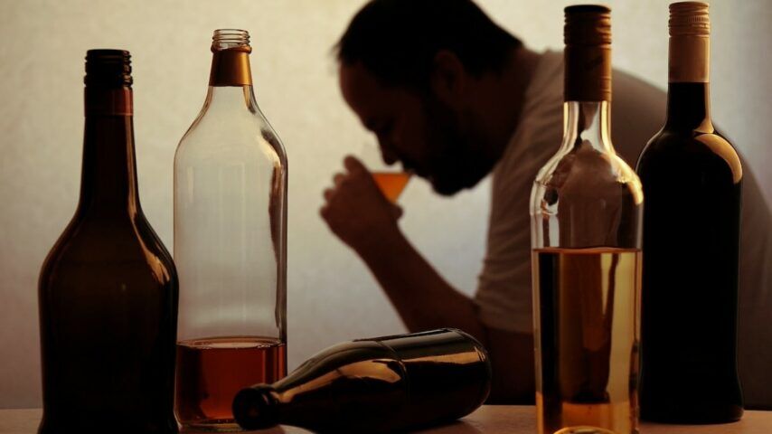 silhouette of anonymous alcoholic person drinking behind bottles of alcohol